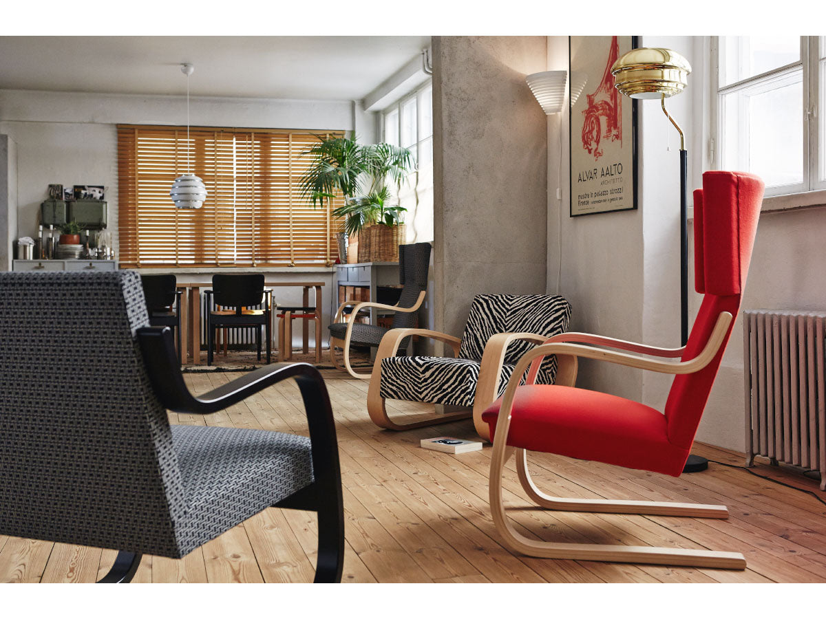Artek A808 Floor Light - A modern living room scene featuring a prominent red upholstered armchair with a curved light wood frame in the foreground, alongside other stylish chairs and a dining area in the background.