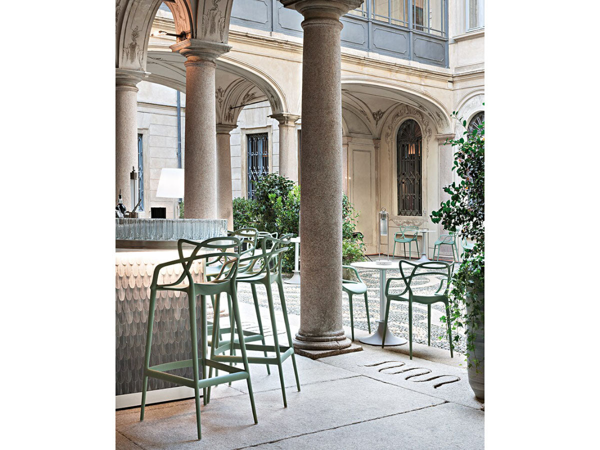 Kartell Masters Stools - Outdoor seating area with sage green chairs and tables in a classical building courtyard.