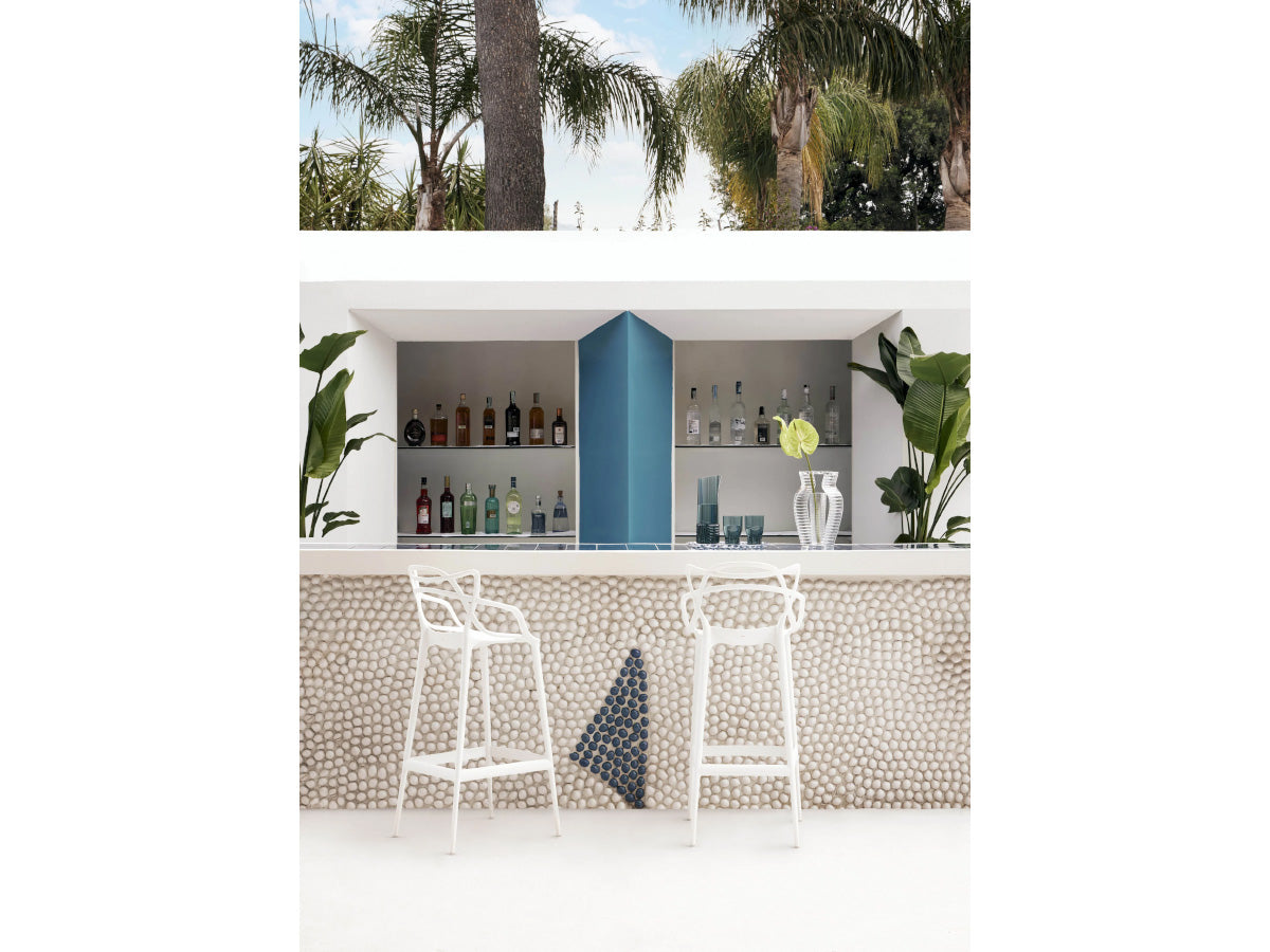 Kartell Masters Stools in Outdoor bar area with palm trees and a blue partition.