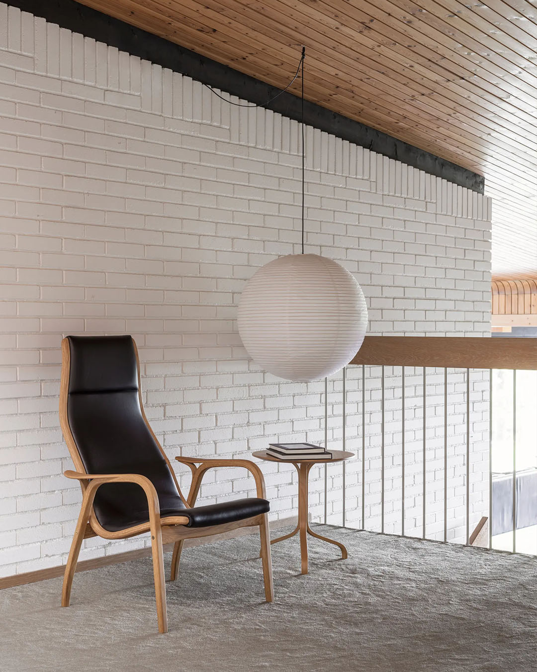 Modern interior with a black leather lamino chair and swedese round table against a white brick wall.